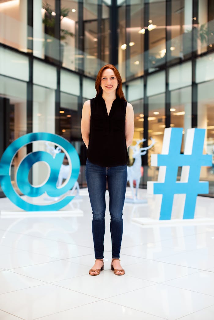 Confident young woman standing in a modern office atrium with digital symbols.